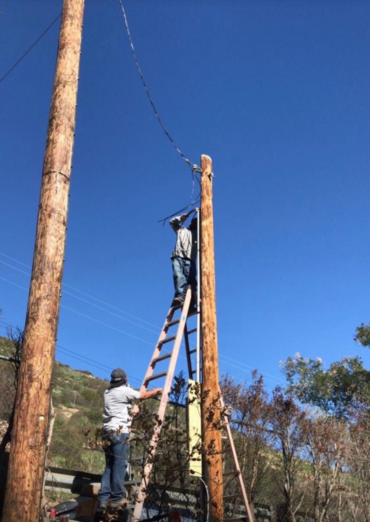 Two technicians working on a utility pole service connection