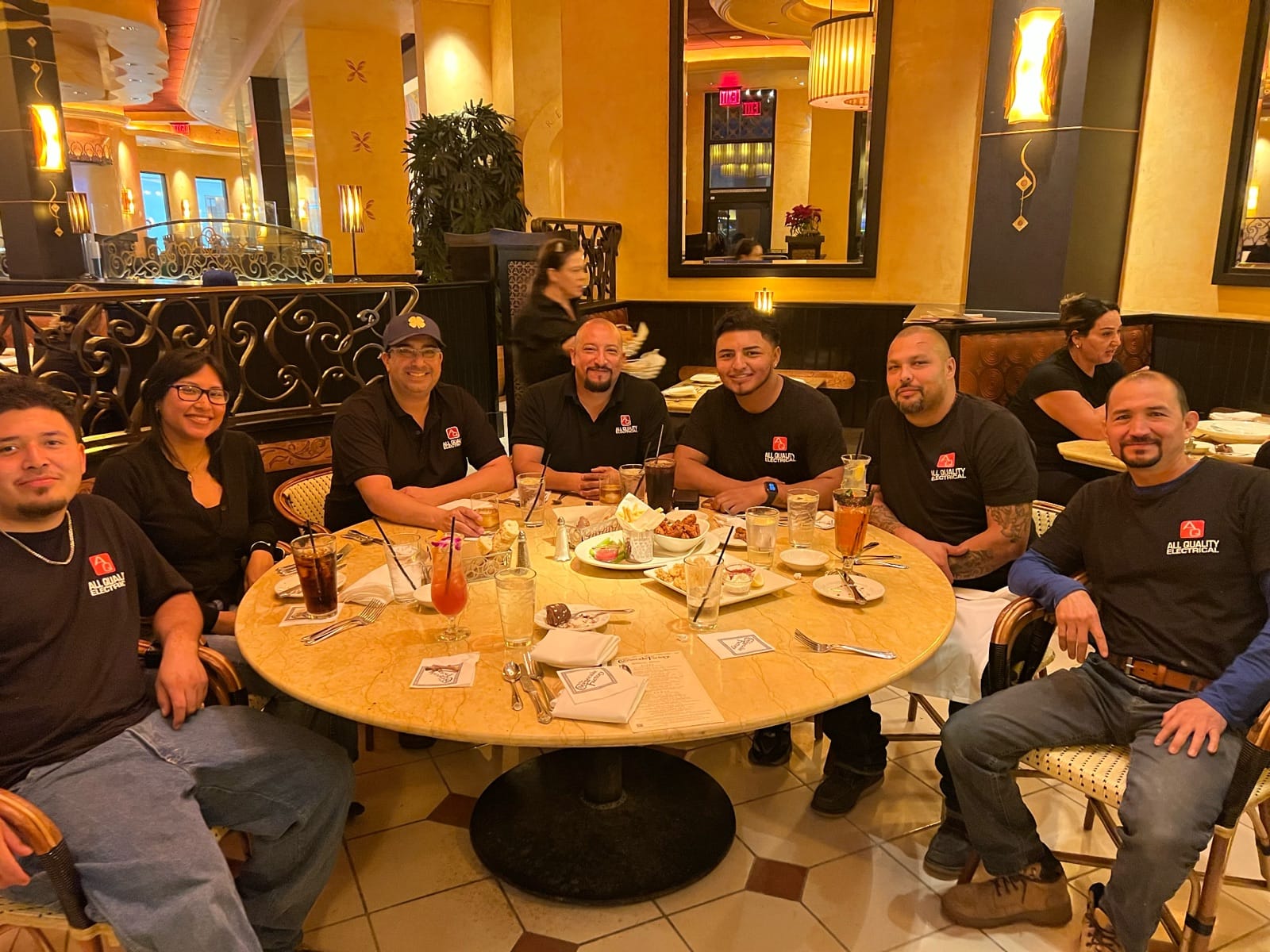 The full AQE crew at a restaurant table, all wearing black AQE shirts